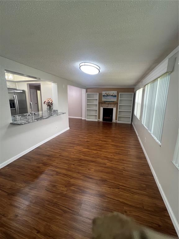 A living room with wood-look flooring, a fireplace, built-in shelves, and a kitchen pass-through window — 4251 100TH AVENUE N, PINELLAS PARK, FL