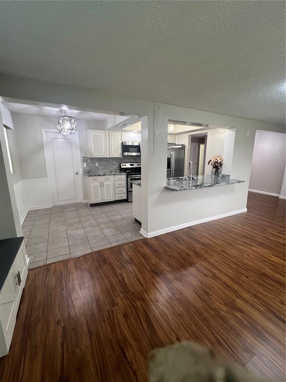 A kitchen with white cabinets and granite countertops overlooks a living area with wood flooring — 4251 100TH AVENUE N, PINELLAS PARK, FL