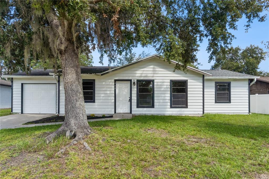A single-story white house with a garage, a large tree, and a grassy front yard — 648 FLORIDIAN DRIVE, KISSIMMEE, FL