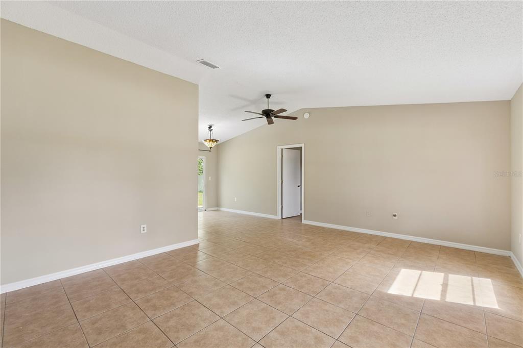 A living room with light-colored tile flooring, white walls, two windows, and a green sofa — 648 FLORIDIAN DRIVE, KISSIMMEE, FL