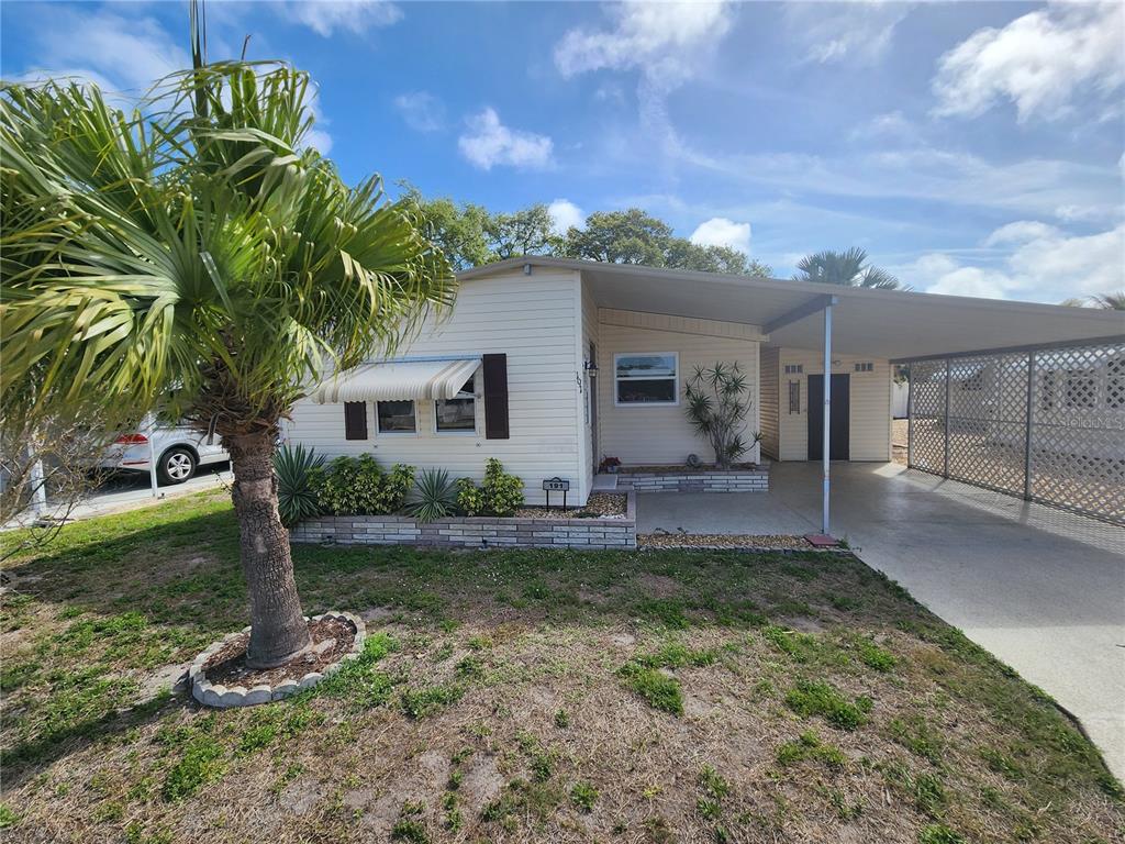 A single-story mobile home with light siding, a palm tree, and an attached carport — 808 53RD AVENUE E UNIT 191, BRADENTON, FL