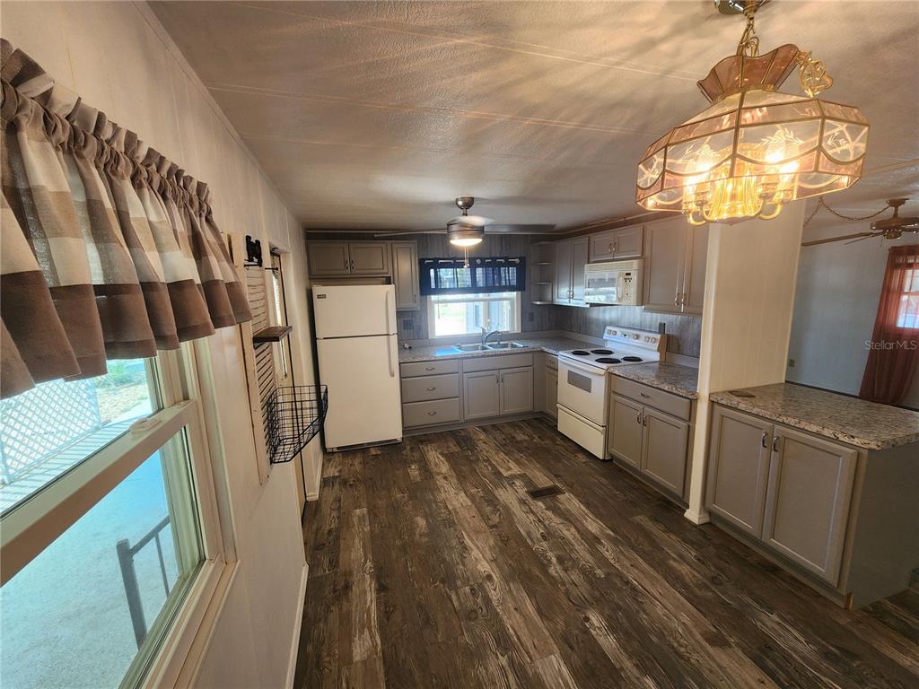 A kitchen with gray cabinets, white appliances, wood-look flooring, and a decorative hanging light fixture — 808 53RD AVENUE E UNIT 191, BRADENTON, FL