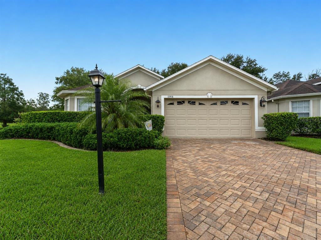 A single-story house with a beige stucco exterior, a brick paver driveway, and manicured hedges — 11916 HERITAGE POINT DRIVE, HUDSON, FL