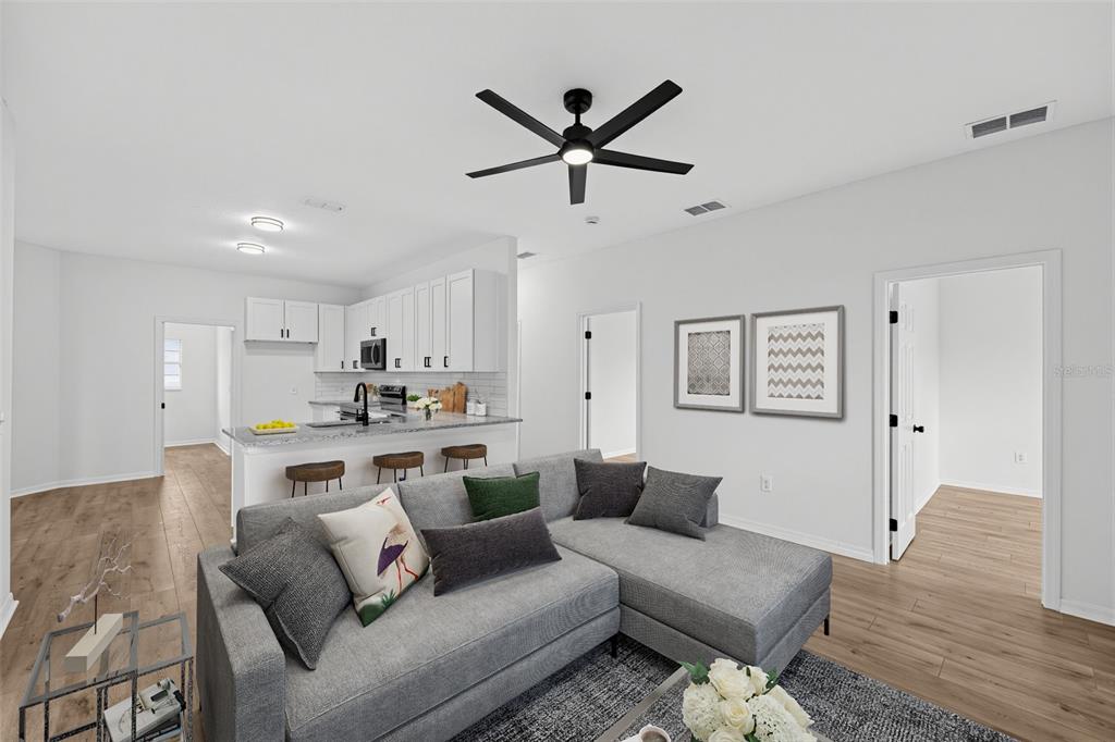 A living room with a gray sectional sofa opens to a kitchen with white cabinets — 507 BRITTEN DRIVE, KISSIMMEE, FL