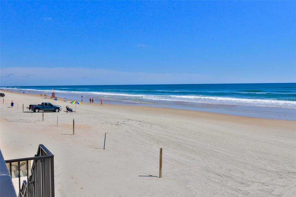 A view of a sandy beach with a parked truck and people near the ocean — 2200 N ATLANTIC AVENUE UNIT 1201, DAYTONA BEACH, FL