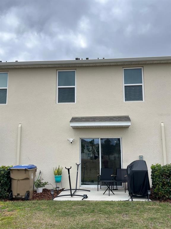 The exterior of a two-story tan stucco building features a sliding glass door and patio — 2755 BRIE HAMMOCK BEND, HARMONY, FL