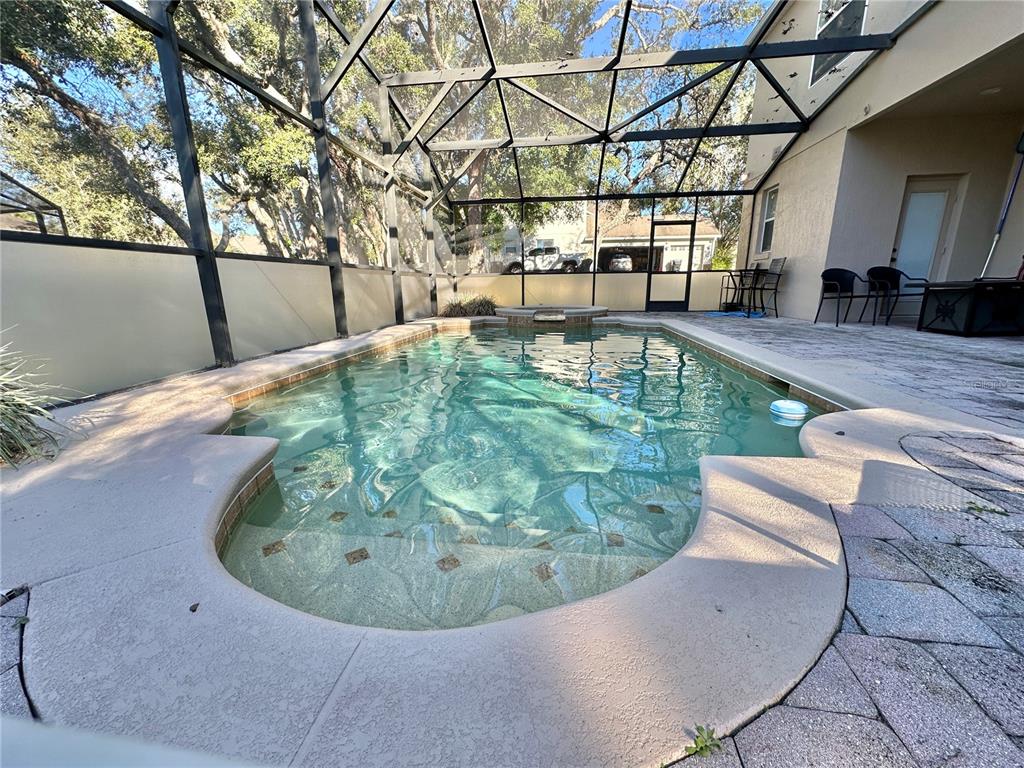 A screened-in swimming pool with a spa and paver patio sits behind a house — 4410 PINE GOLD AVENUE, APOPKA, FL
