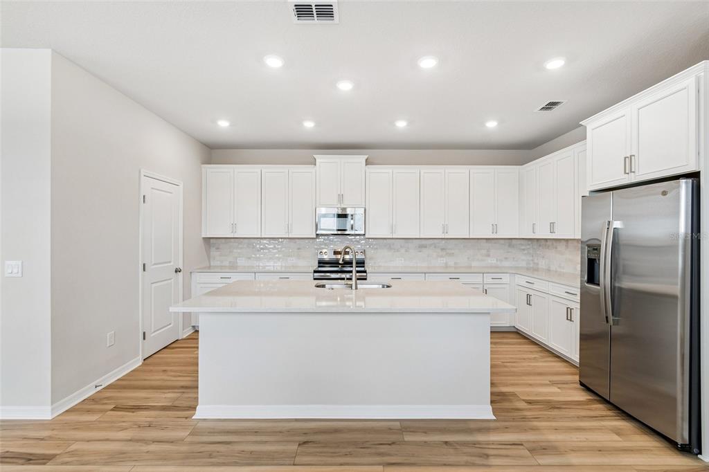 A modern kitchen features white cabinetry, a central island, stainless steel appliances, and wood flooring — 5640 SAVANNA VALLEY TRAIL, ST CLOUD, FL
