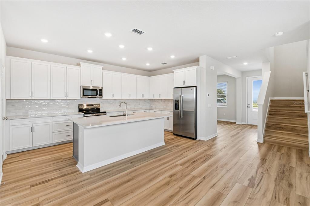 A modern kitchen features white cabinets, stainless steel appliances, a center island, and wood flooring — 5640 SAVANNA VALLEY TRAIL, ST CLOUD, FL