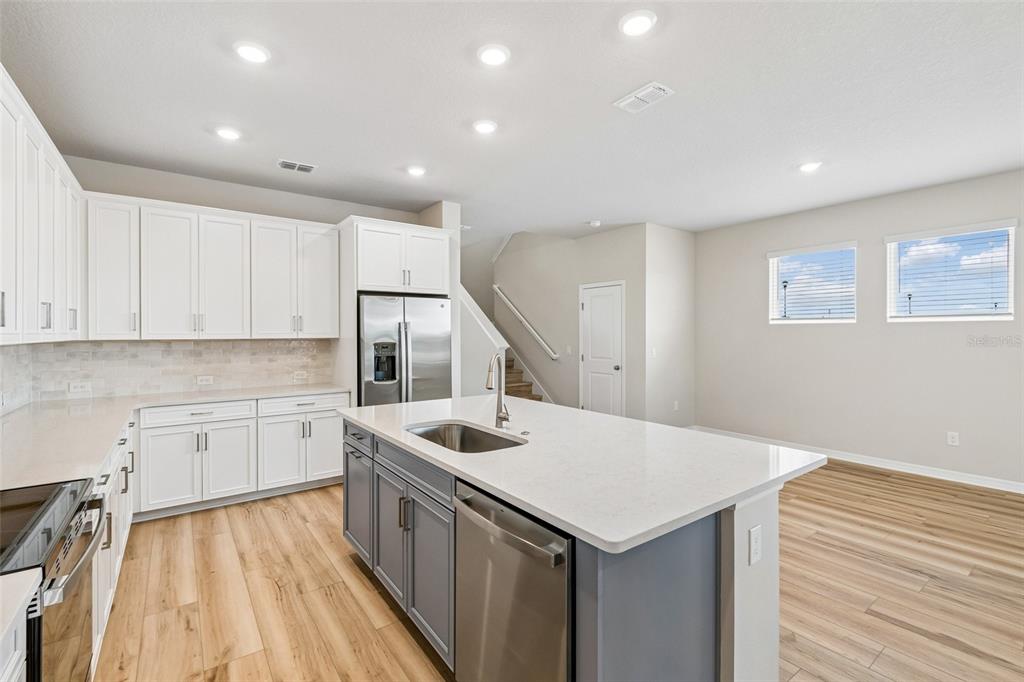 A modern kitchen features white upper cabinets, gray lower island cabinets, and light wood flooring — 5640 SAVANNA VALLEY TRAIL, ST CLOUD, FL