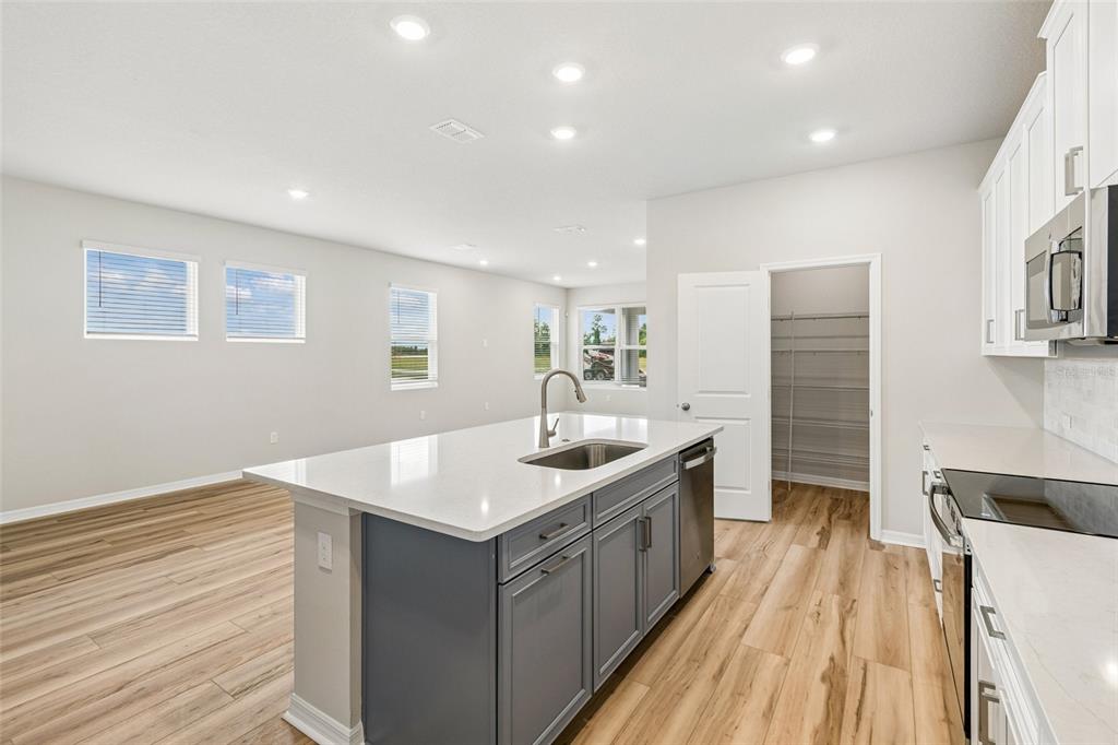 A kitchen features a gray island with a sink, white cabinets, and light wood flooring — 5640 SAVANNA VALLEY TRAIL, ST CLOUD, FL