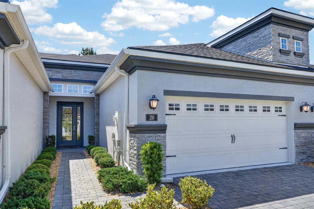 A modern house exterior features a stone-accented facade, a white garage door, and a walkway — 20 LONGRIDGE LANE, ORMOND BEACH, FL