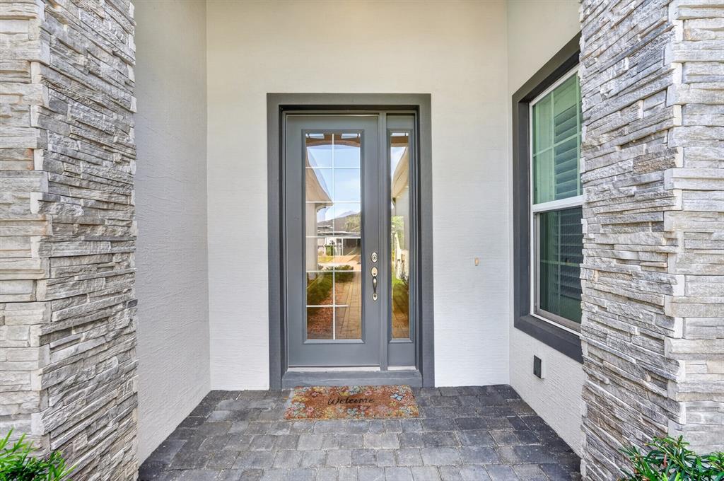 A front entryway features a gray door with glass panels, stone pillars, and paver flooring — 20 LONGRIDGE LANE, ORMOND BEACH, FL