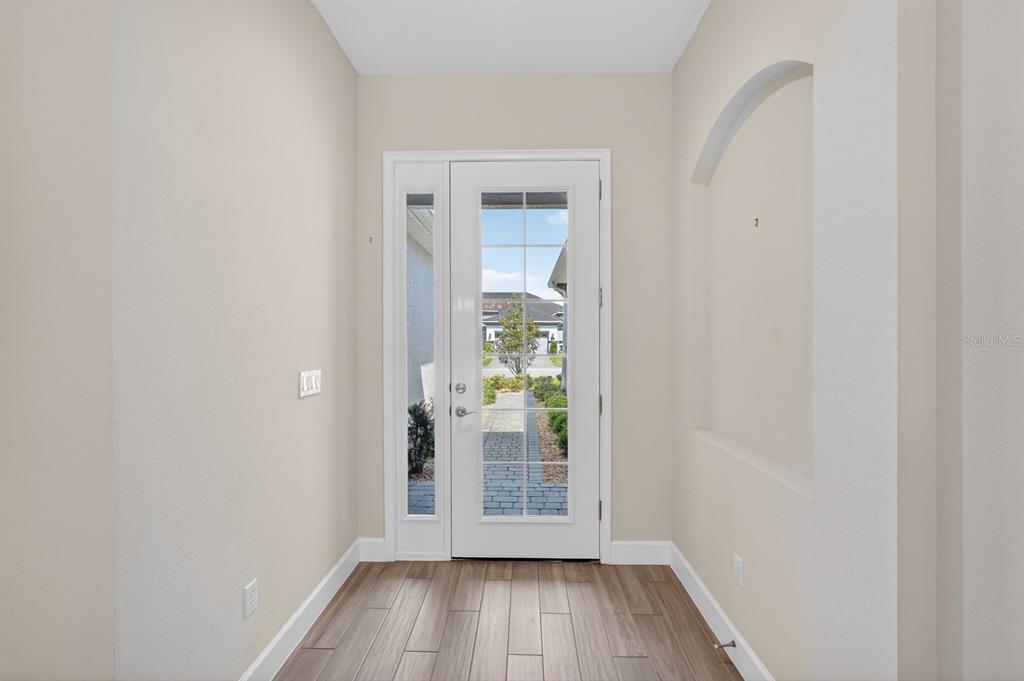 A bright entryway features wood-look tile flooring, light beige walls, and a glass-paneled front door — 20 LONGRIDGE LANE, ORMOND BEACH, FL