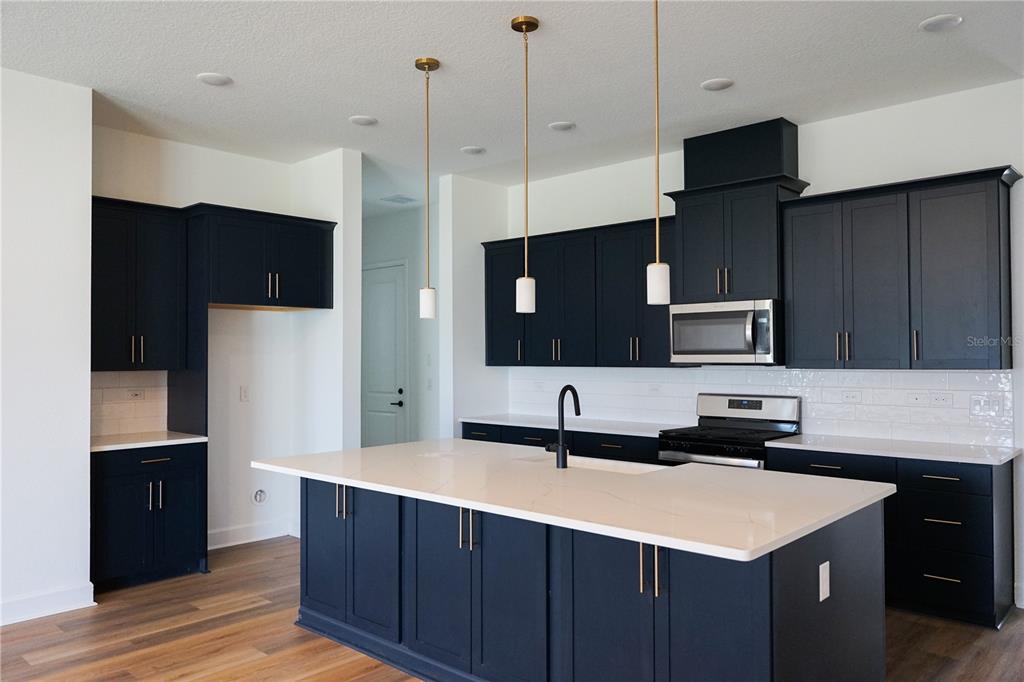 A modern kitchen features dark blue cabinets, a large white island, and gold pendant lighting — 1 BLUE GROTTO PLACE, PALM COAST, FL