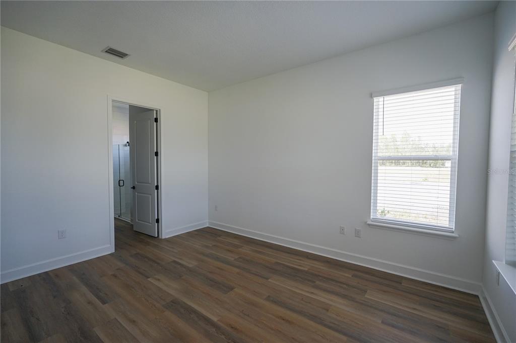 An empty bedroom features wood-look flooring, white walls, a window with blinds, and an open doorway — 1 BLUE GROTTO PLACE, PALM COAST, FL