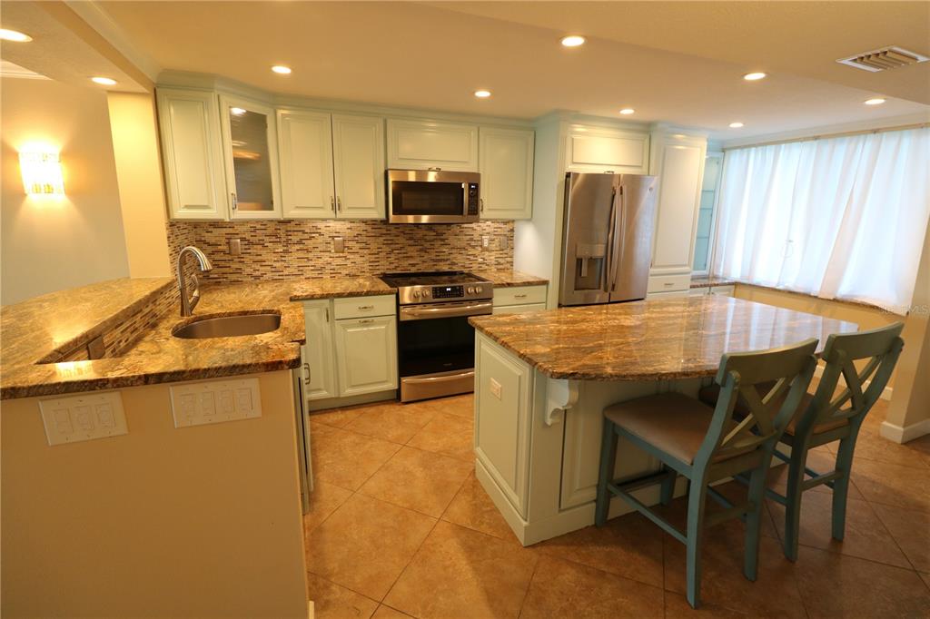 A kitchen features light blue cabinets, granite countertops, a center island, and stainless steel appliances — 9495 BLIND PASS ROAD UNIT 504, ST PETE BEACH, FL