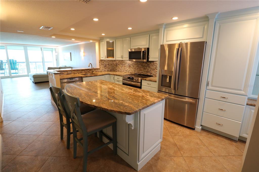 A kitchen with light blue cabinets, granite countertops, a center island, and stainless steel appliances — 9495 BLIND PASS ROAD UNIT 504, ST PETE BEACH, FL