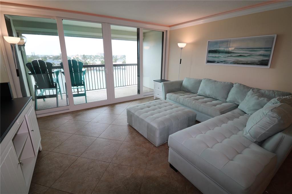 A living room features a light-colored sectional sofa, a matching ottoman, tile flooring, and a balcony — 9495 BLIND PASS ROAD UNIT 504, ST PETE BEACH, FL