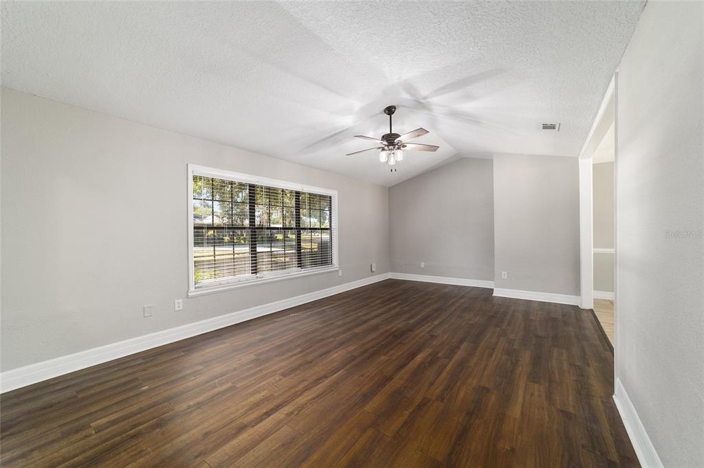 An empty living room features dark wood-look flooring, light gray walls, and a ceiling fan — 35 PINE CIRCLE, OCALA, FL