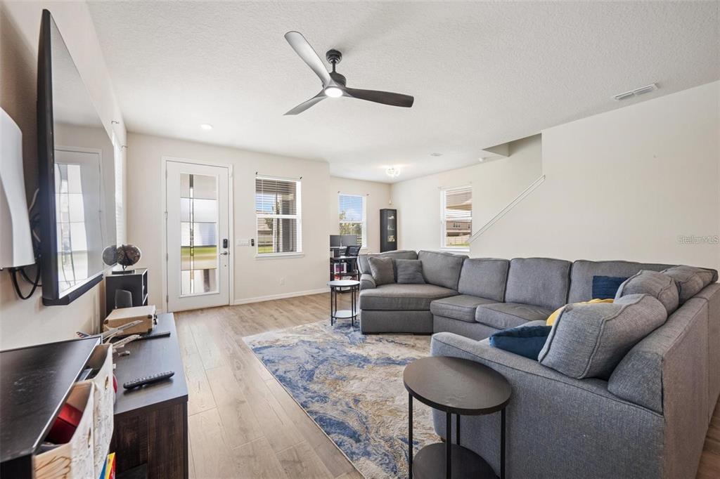 A living room features a gray sectional sofa, a blue patterned rug, and wood-look flooring — 2769 FRANKLIN ROAD, ST CLOUD, FL