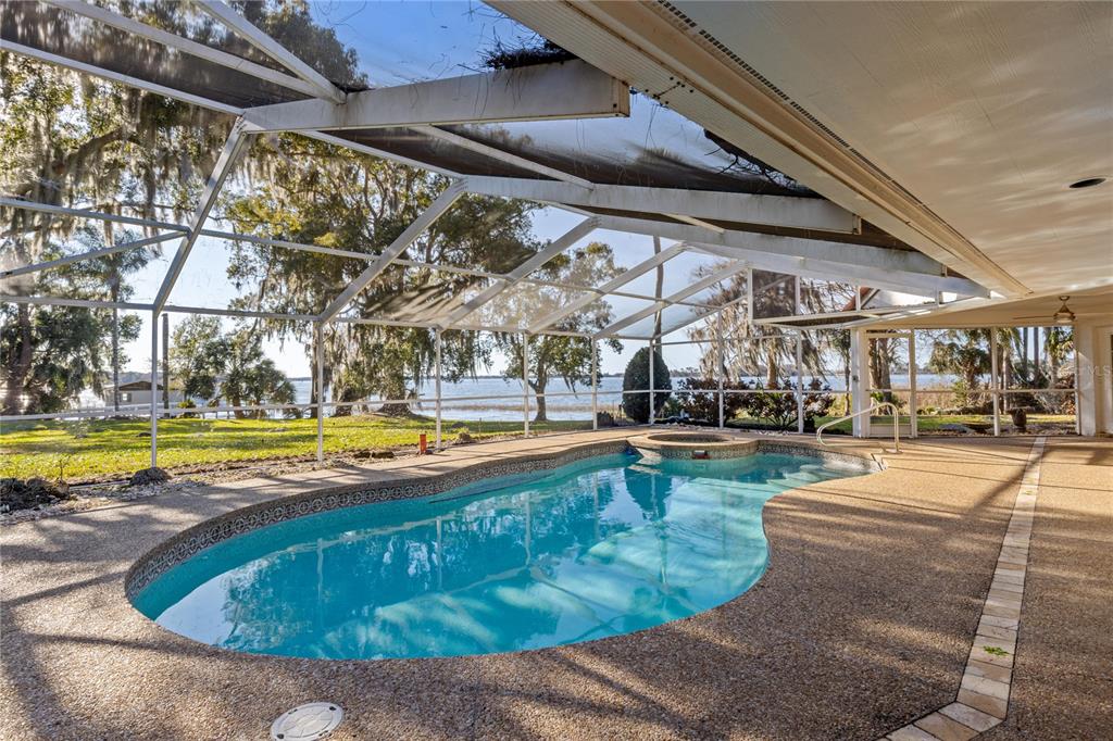 A screened-in pool and spa overlook a lake from a covered patio — 6136 DORA DRIVE, MOUNT DORA, FL