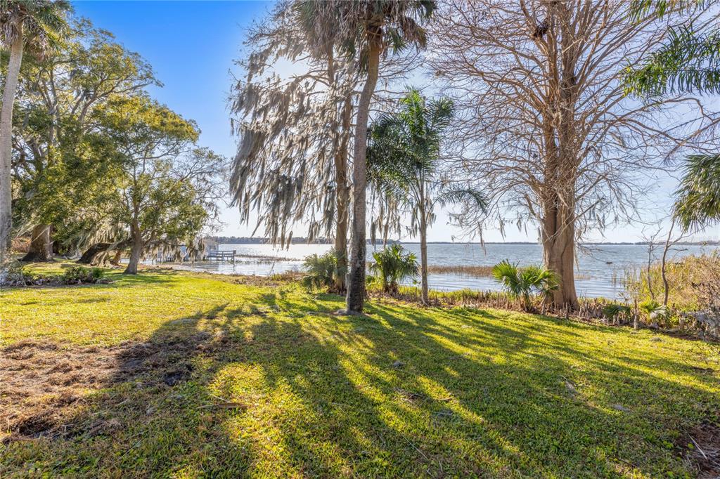 A grassy yard with mature trees leads to a view of a lake — 6136 DORA DRIVE, MOUNT DORA, FL