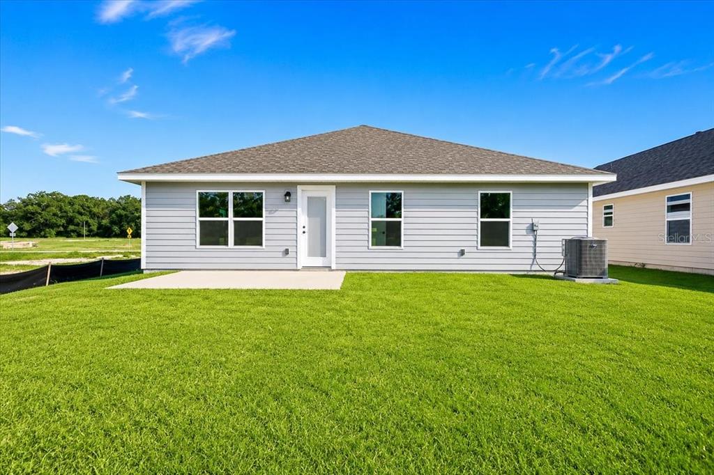 The exterior rear view of a single-story house features light gray siding and a concrete patio — 2585 SW 250TH DRIVE, NEWBERRY, FL