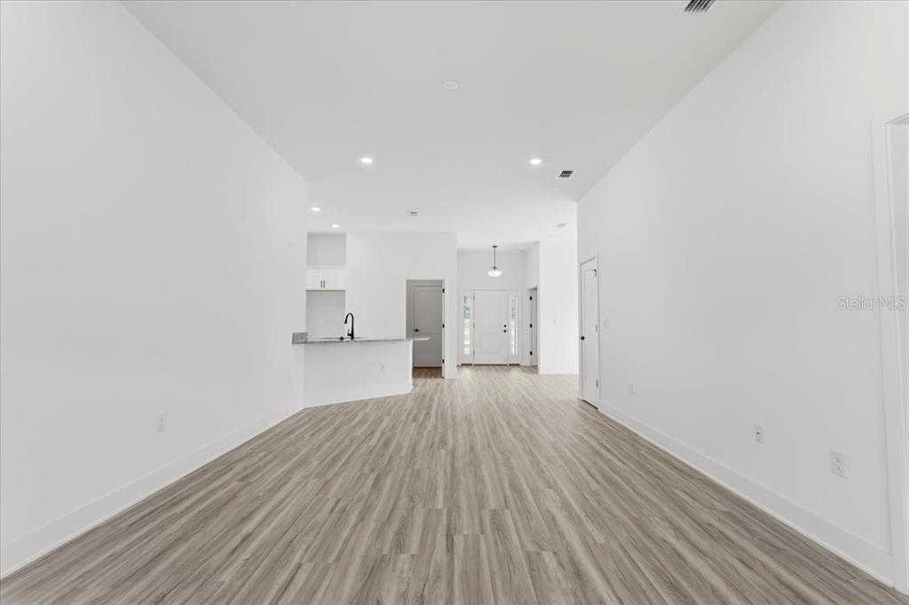 A bright, open-concept living area features white walls, light wood-look flooring, and a kitchen peninsula — 2585 SW 250TH DRIVE, NEWBERRY, FL