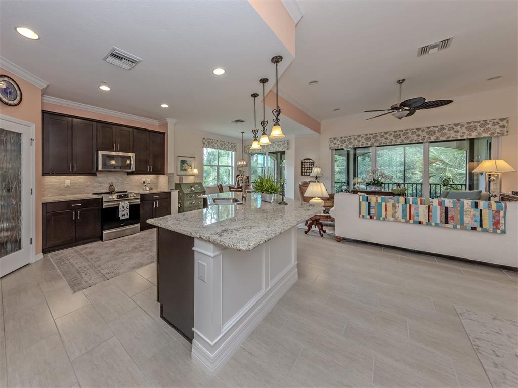 A kitchen with dark cabinets and a granite island opens into a living area — 170 BELLA VISTA TERRACE UNIT 20C, NORTH VENICE, FL