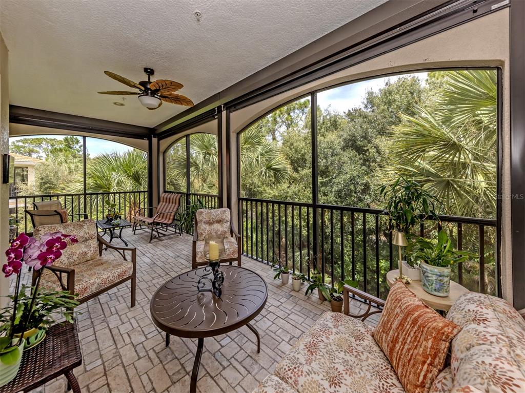 A screened-in balcony features brick flooring, patio furniture, a ceiling fan, and views of trees — 170 BELLA VISTA TERRACE UNIT 20C, NORTH VENICE, FL