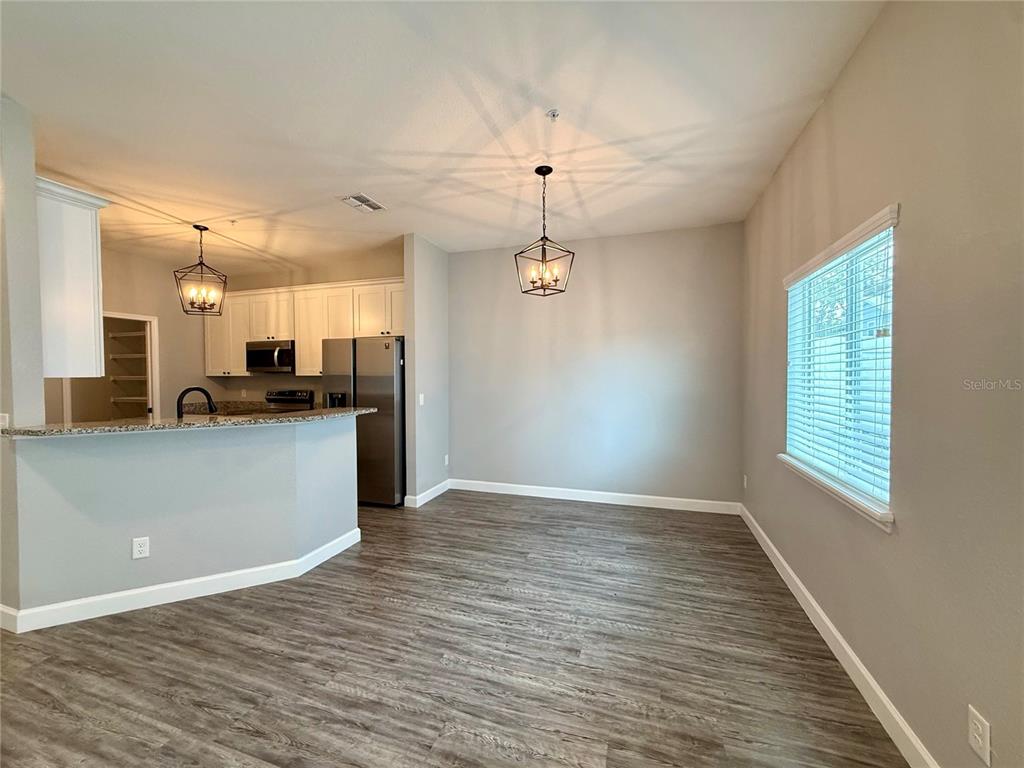 An open-concept kitchen and dining area features white cabinets, stainless steel appliances, and wood-look flooring — 2430 WILLOW WAY, WINTER HAVEN, FL