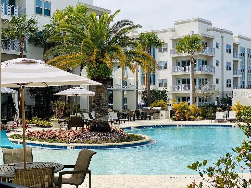 A swimming pool with a central palm tree island sits before a multi-story apartment building — 1688 CELEBRATION BOULEVARD UNIT The Audrey, CELEBRATION, FL