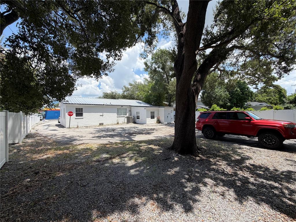 A white single-story building sits on a gravel lot with a large tree and red SUV — 3714 W HORATIO STREET, TAMPA, FL