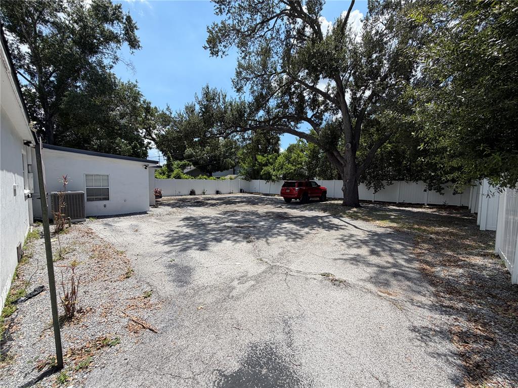 A large, cracked asphalt parking area sits beside a white building under a large tree — 3714 W HORATIO STREET, TAMPA, FL