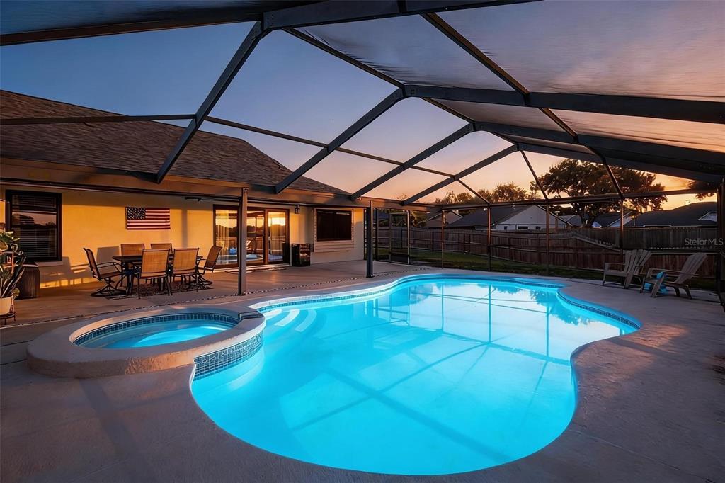 A screened-in patio features a swimming pool with an integrated spa at sunset — 1917 REDBRIDGE DRIVE, BRANDON, FL