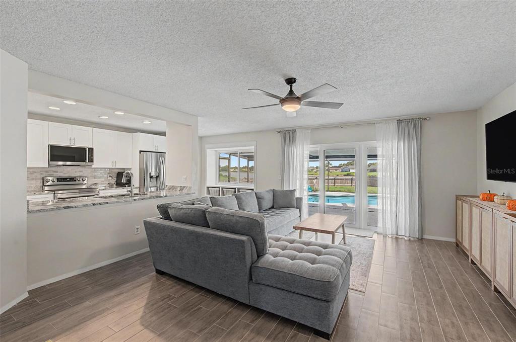 A living room with a grey sectional sofa, wood-look tile floors, and a view of a pool — 1917 REDBRIDGE DRIVE, BRANDON, FL