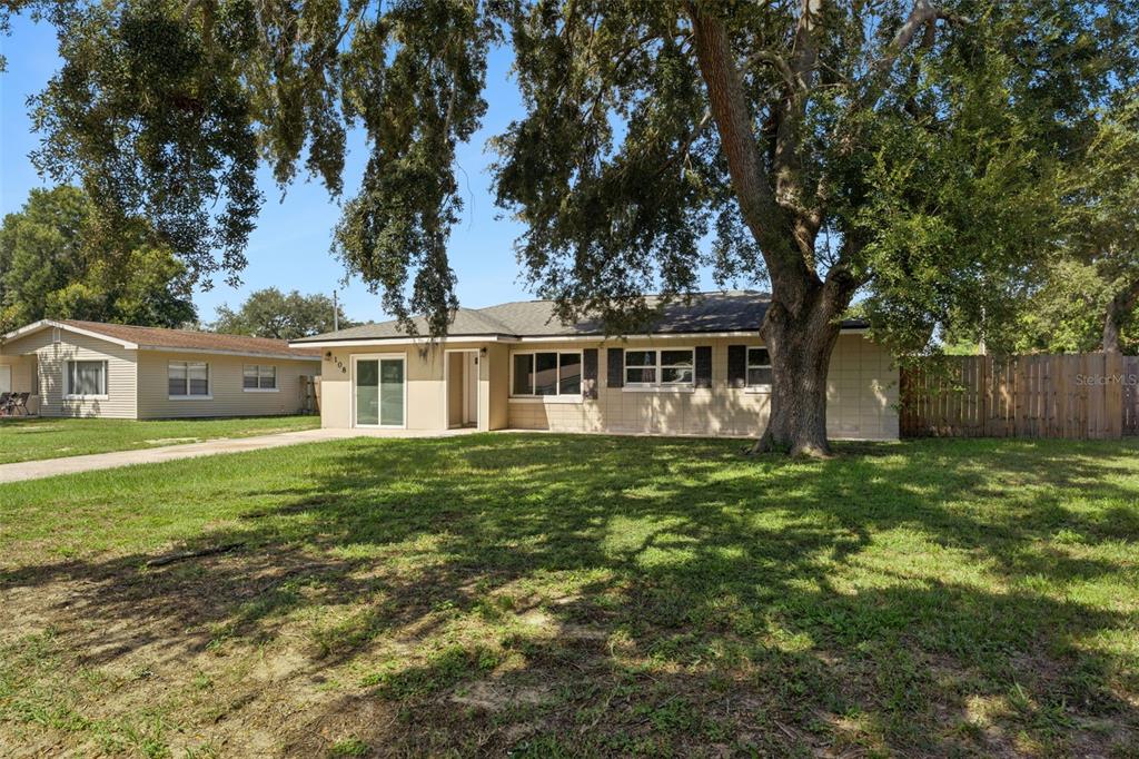 A single-story house with a beige exterior, a large oak tree, and a wooden fence — 108 ALEXANDRIA AVENUE, MINNEOLA, FL