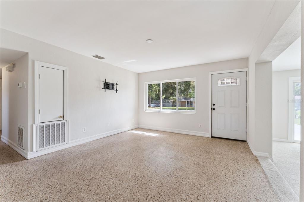 An empty room with beige speckled flooring, a white front door, and a large window — 108 ALEXANDRIA AVENUE, MINNEOLA, FL