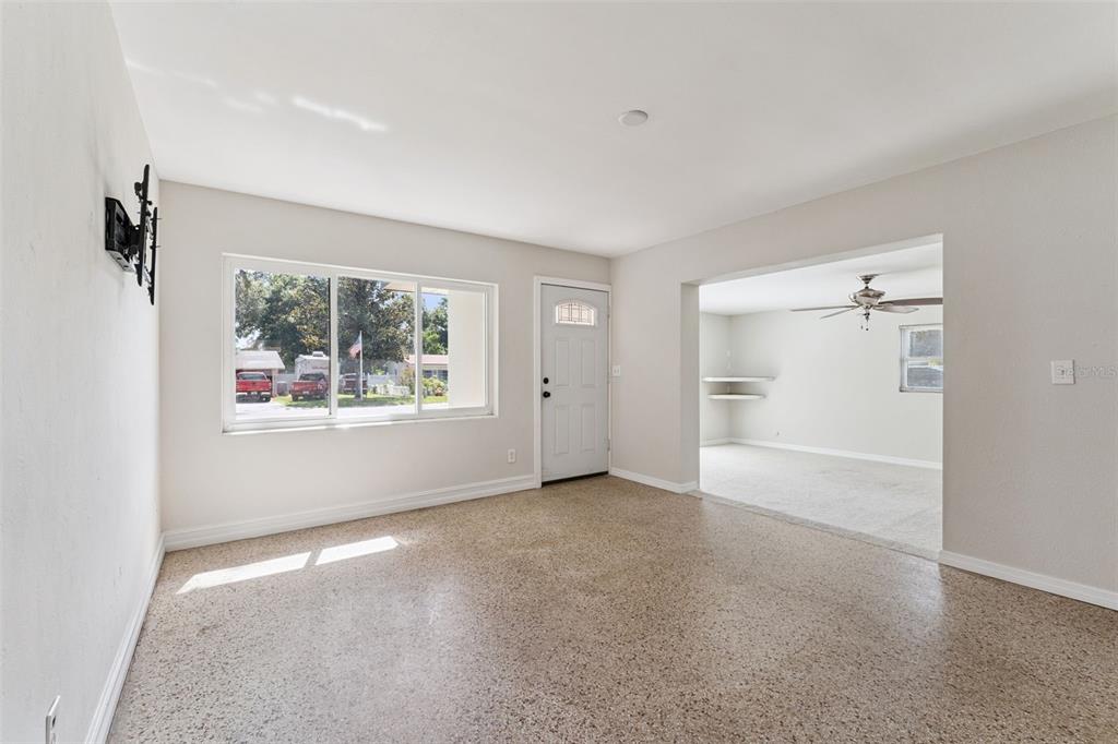 A living room with terrazzo flooring, a large window, and an entryway to a carpeted room — 108 ALEXANDRIA AVENUE, MINNEOLA, FL