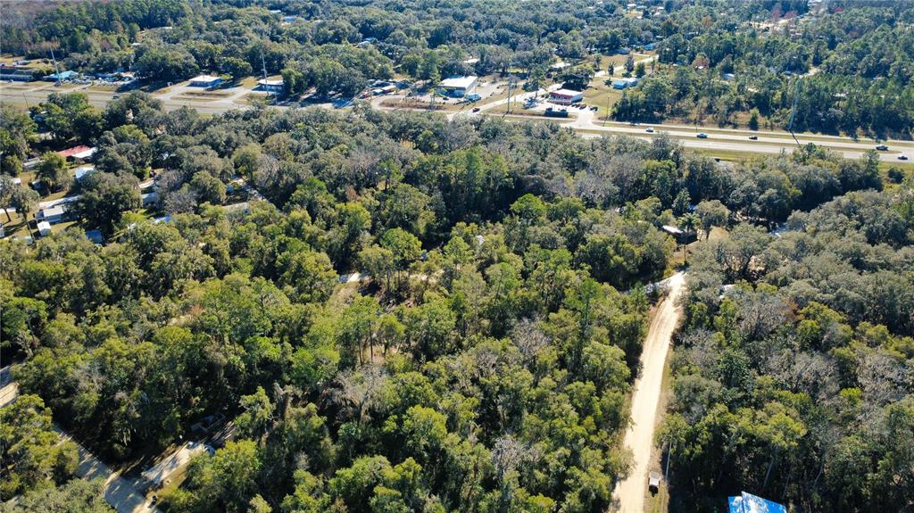 An aerial view shows a wooded lot with a dirt road and nearby highway — 110 LEEWARD ROAD, SATSUMA, FL