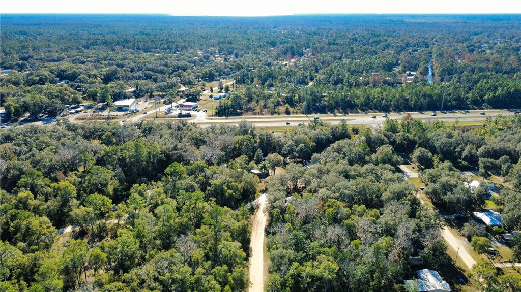 An aerial view shows a wooded lot with a dirt road and a nearby highway — 110 LEEWARD ROAD, SATSUMA, FL