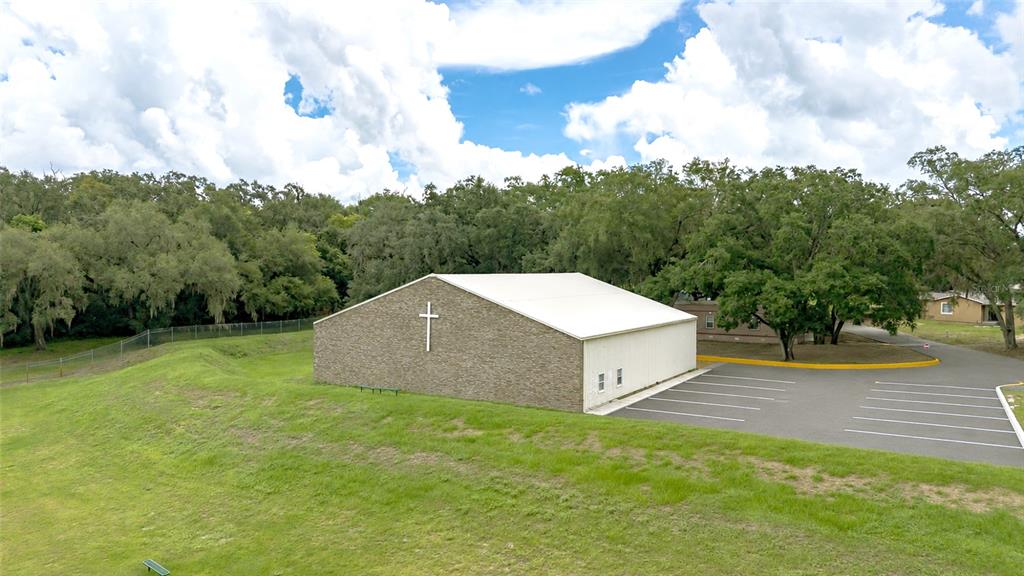 An exterior view of a church building with a stone facade, cross, and adjacent parking lot — 6837 LAKEVILLE ROAD, APOPKA, FL