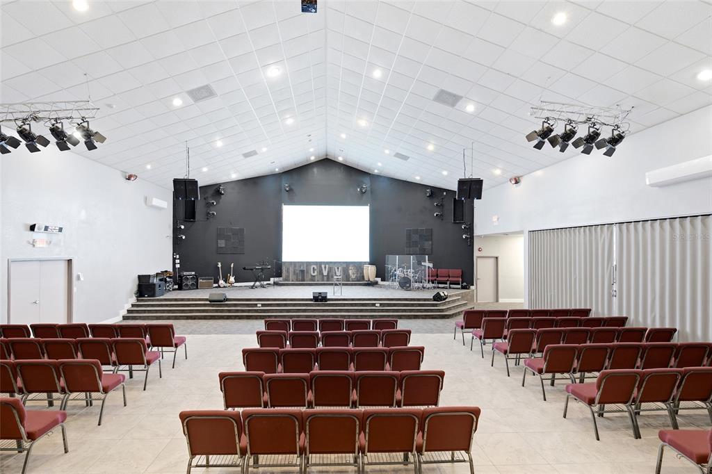 A church sanctuary features rows of red chairs facing a stage with a projection screen — 6837 LAKEVILLE ROAD, APOPKA, FL