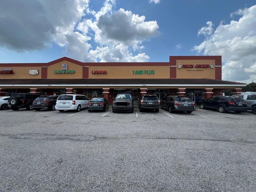 A strip mall exterior features multiple storefronts with parked cars in a paved parking lot — 2064 E OSCEOLA PARKWAY UNIT 102, KISSIMMEE, FL