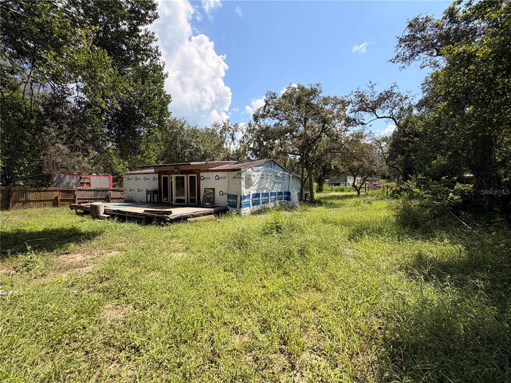 A small, unfinished house with a wooden deck sits in a grassy, tree-filled lot — 16100 SE 253RD COURT, UMATILLA, FL
