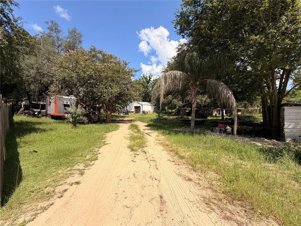 A dirt driveway leads toward a small white building on a grassy, tree-lined lot — 16100 SE 253RD COURT, UMATILLA, FL