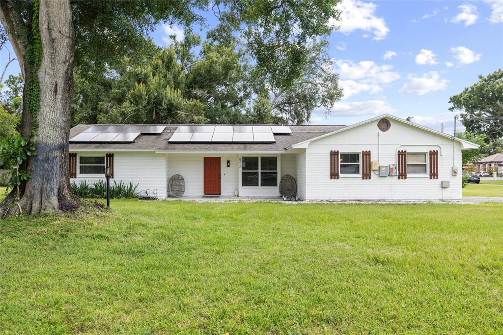 A single-story white brick house features a red front door and roof-mounted solar panels — 8212 SUNNY VALE PLACE, TAMPA, FL