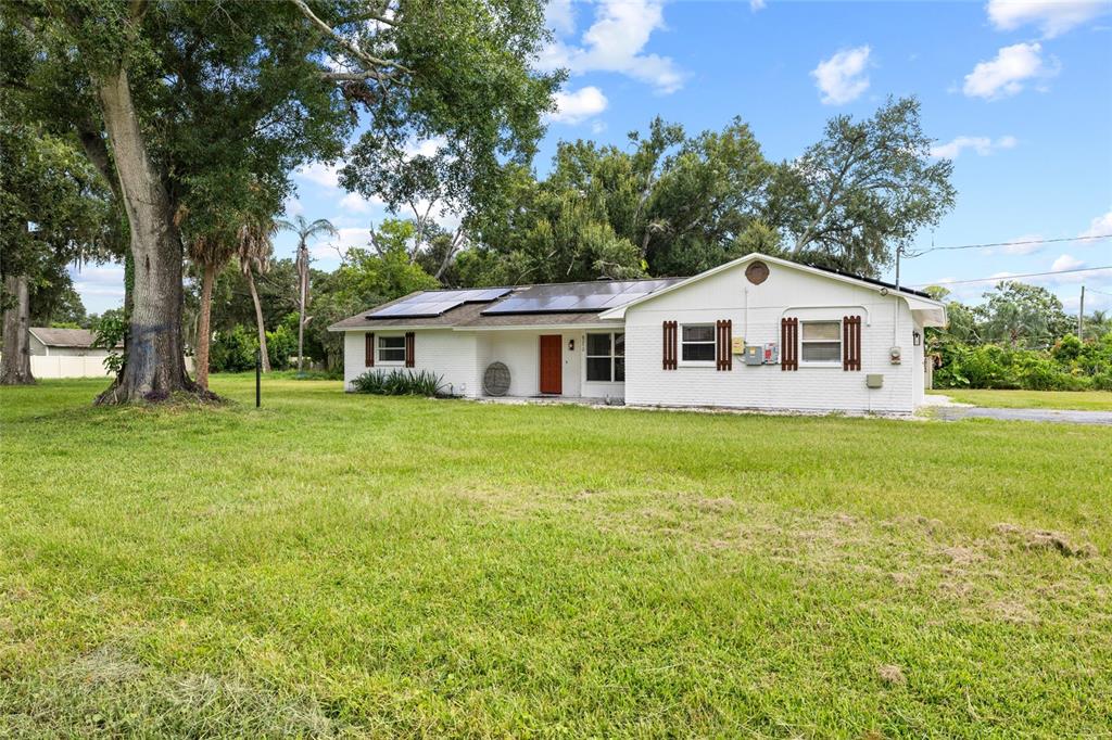 A single-story white house with solar panels and a large lawn under a blue sky — 8212 SUNNY VALE PLACE, TAMPA, FL
