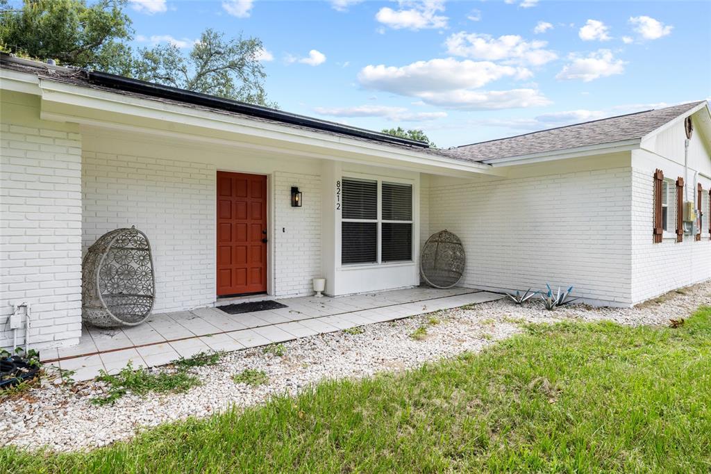 A white brick house exterior features a red front door and two hanging egg chairs — 8212 SUNNY VALE PLACE, TAMPA, FL